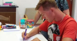 Mladý muž píše fixem u stolu během individuální ergoterapie v centru Sarema