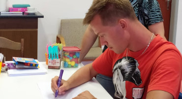 Mladý muž píše fixem u stolu během individuální ergoterapie v centru Sarema
