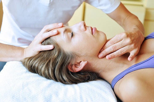 Terapeut provádí osteopatické ošetření krční páteře u ležící ženy.