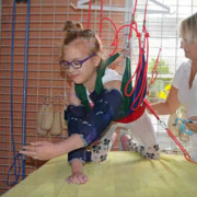 Dívka s brýlemi cvičí v závěsném systému pod dohledem terapeuta