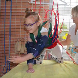 Dívka s brýlemi cvičí v závěsném systému pod dohledem terapeuta