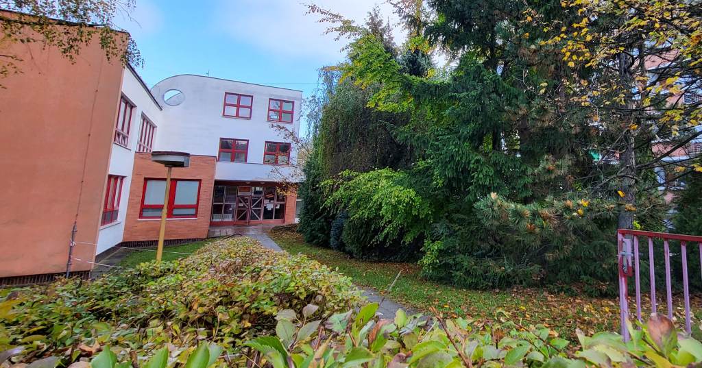 Pohled na vchod do bílo-oranžové budovy rehabilitačního centra, lemovaný zelení a stromy.