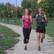 Žena a muž běží po štěrkové cestě v parku, obklopeni zelení.