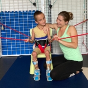 Chlapec v rehabilitačním obleku v kleci Spider s fyzioterapeutkou, která ho podporuje a usmívá se na něj.