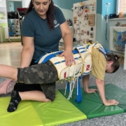 Fyzioterapeutka pomáhá dívce v rehabilitačním obleku při cvičení na podložce v terapii TheraSuit