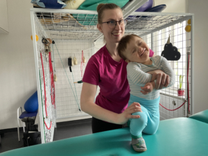 Fyzioterapeutka cvičí s usměvavým dítětem v rehabilitační kleci.