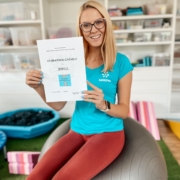 Usměvavá žena v tyrkysovém tričku SAREMA sedí na gymnastickém míči a drží certifikát ochranné známky