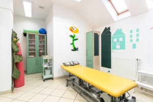 Dětská fyzioterapeutická ordinace s barevnou výmalbou, lehátkem a úložným nábytkem.