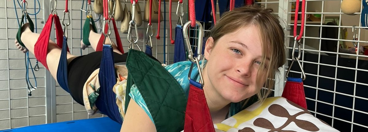 Dívka ležící v závěsném terapeutickém systému s barevnými popruhy s barevným polštářem.